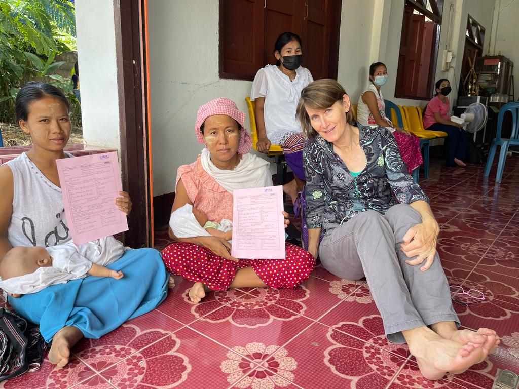 Rose is pictured with two mothers, cradling their newborn babies and holding their birth certificates which is one of the many benefits of birthing in the clinics rather than at home.